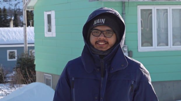 A man stands outside in winter, wearing a heavy jacket and a tuque with the word Nain stitched on.