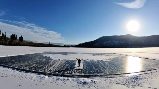 A person stands on top of a giant Canadian flag carved into the snow of a frozen lake.