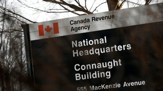 A sign, slightly obscured by barren branches from a bush, reads "Canada Revenue Agency, National Headquarters."