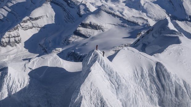 An aerial shot of a snow-covered mountain top with two tiny people at the summit.