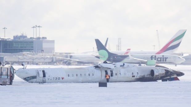 Snow-covered airplane lies on its side at a snowy airport. Emergency personnel are inspecting it. 