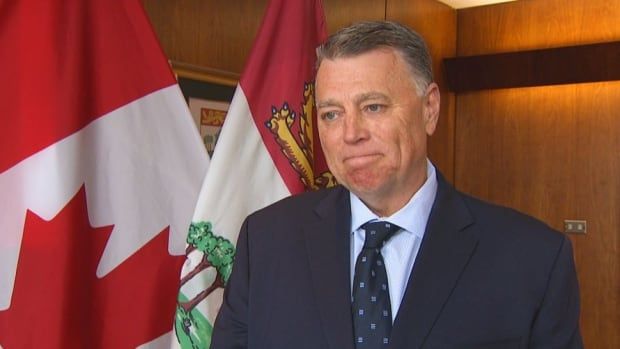 Man with blue jacket and tie standing in front of Canadian flag.