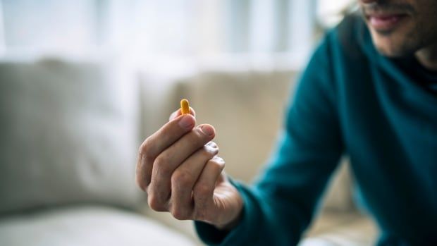 Close-up of man holding yellow pill.