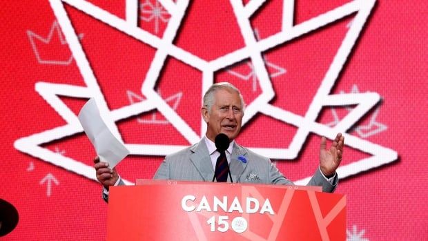 A person stands at a podium with a sign reading 'Canada 150' on it. Behind them, a maple leaf is outlined in white against a red background.