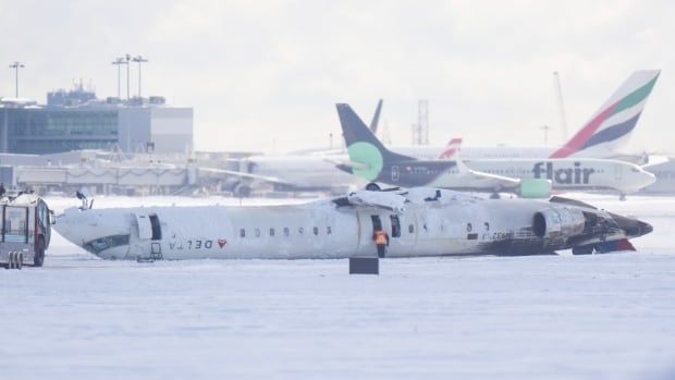 On a snowy winter day, an airplane lies overturned on a runway in Toronto