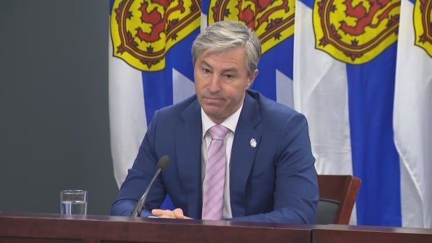 Man sits at desk with flag behind him.