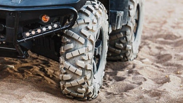 A closeup shows the tires of an all-terrain vehicle on sandy ground.