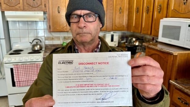 A man standing in a kitchen and holding a power disconnect notice. He is looking at the camera. 