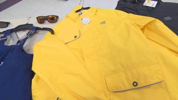 Yellow rain coat on hanger beside a pair of sunglasses and blue rain paints