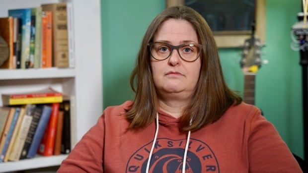 Woman wearing an orange hoodie poses in front of a bookshelf