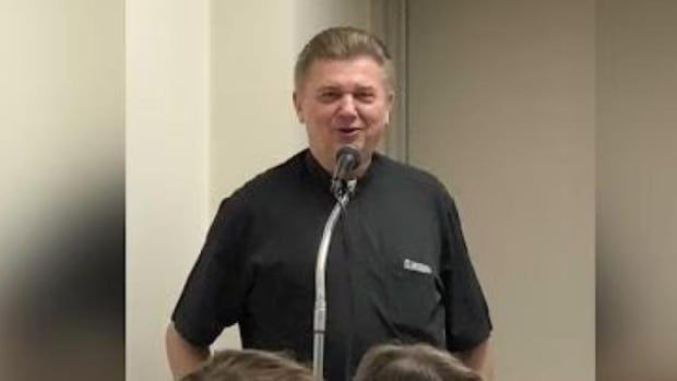 Man stands behind microphone in black t-shirt.