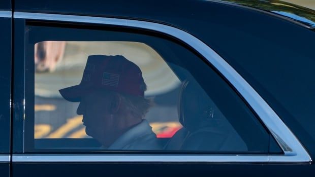 A person wearing a baseball cap is seen sitting in the back of a car.