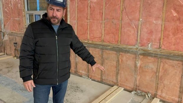 A man wearing a hard hat stands in an unfinished room