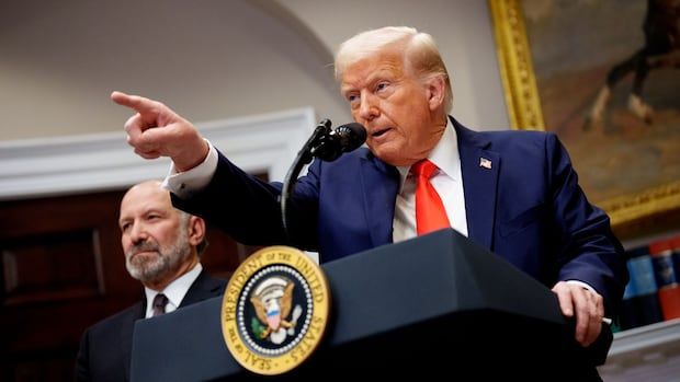 A man in a suit with a red tie, gesturing firmly, speaks at a podium bearing the presidential seal. Another man stands in the background, observing.