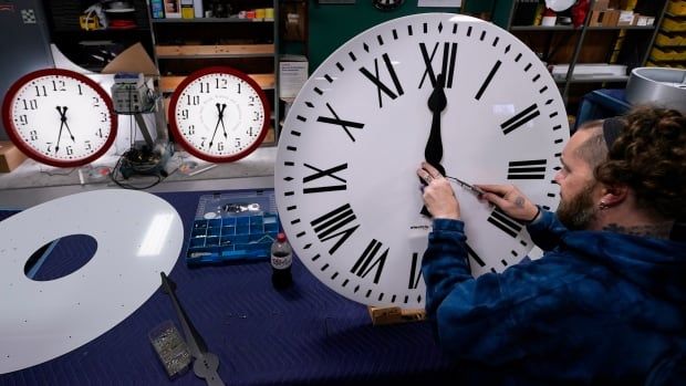 A man adjusts the hands of a large white analog clock.