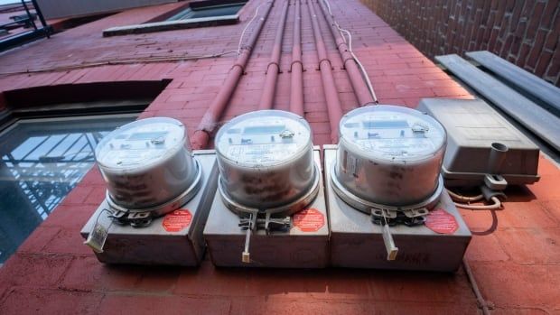 A low-angle shot shows four hydro meters on the side of a red brick building.