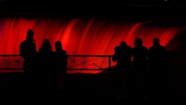 silhouettes of people looking at the falls, lit up in red