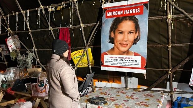 A woman wearing a toque and a cream-coloured coat looks at an image of another woman with the name Morgan Harris on it.