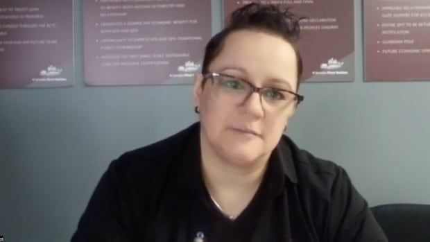 A woman wearing a black top and glasses speaks in front of plaques.