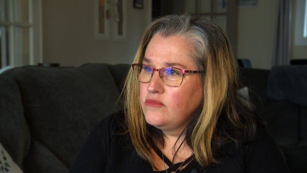 A woman with a concerned look on her face sits on a couch in her living room.