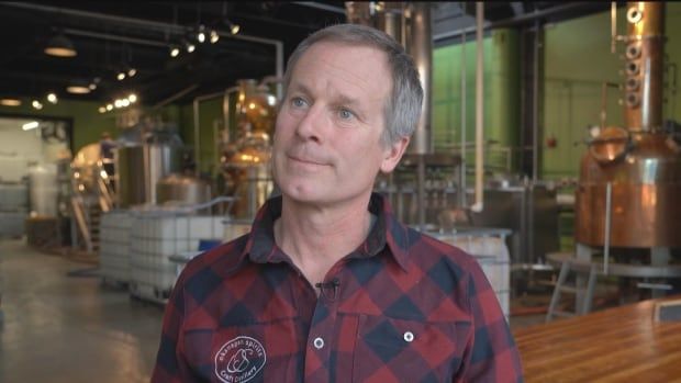 A man wearing a checked shirt speaks in a distillery.