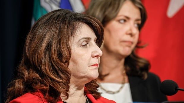 Close-up: a woman stares rightward as another woman behind her gazes in same direction