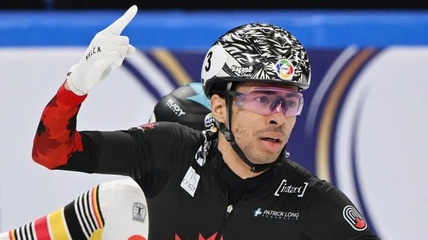 A speed skater points his finger upward in celebration.