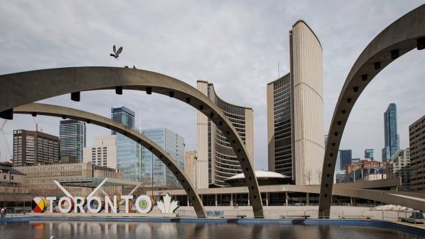 Toronto City Hall is pictured on April 3, 2023. See view across water fountain/pond, past Toronto sign to city hall building in background.