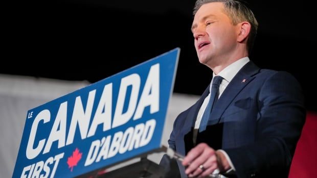 A brown-haired man in a blue suit stands a podium with the words Canada First printed on them.