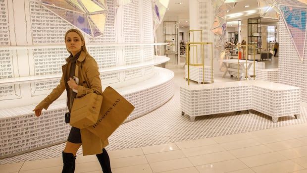 A woman walks in front of empty shelves carrying brown bags.