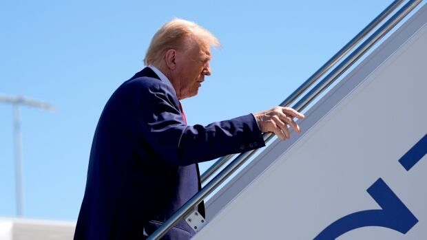 A person hold the railing as they walk up stairs leading to an airplane.