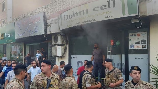 Six Lebanese soldiers in uniform gather outside a smoking, damaged mobile shop.