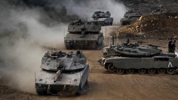 Four tanks are shown in a photograph, kicking up dust and dirt as they travel.