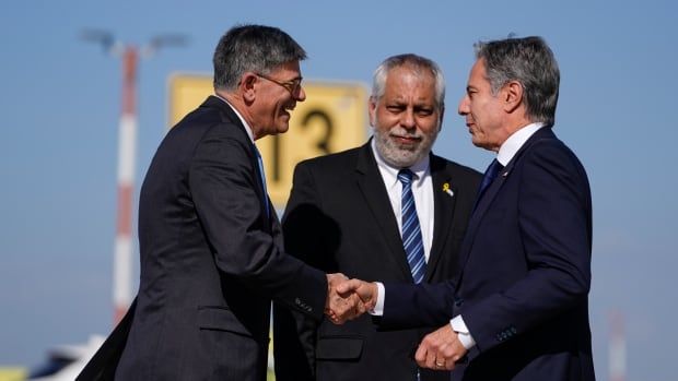 Three men in suits greet each other on a  tarmac