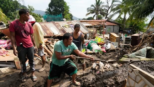 A man stands on top of a pile ruble from a landslide and uses a shovel while others watch.