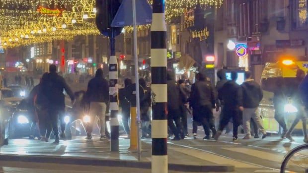 A crowd of people swarm at night on an urban street.