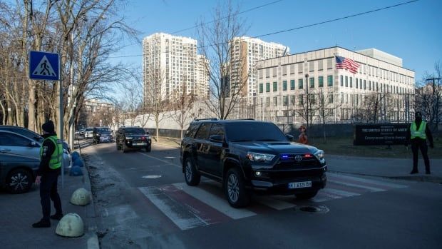 A black SUV drives past a white stone building with a U.S. flag out front.