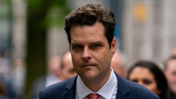 A brown-haired man in a blue suit with a red tie walks into a courthouse.