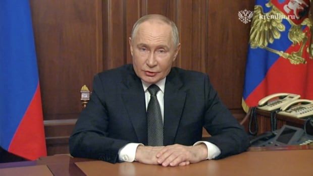 A person sits at a desk with a flag over their left shoulder.