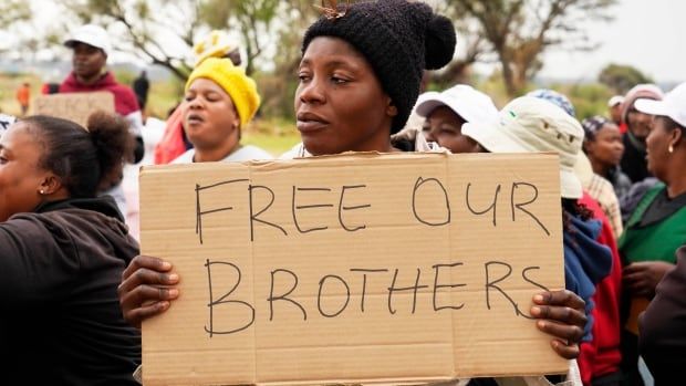 A woman in a crowd holds a cardboard sign that reads: Free Our Borthers