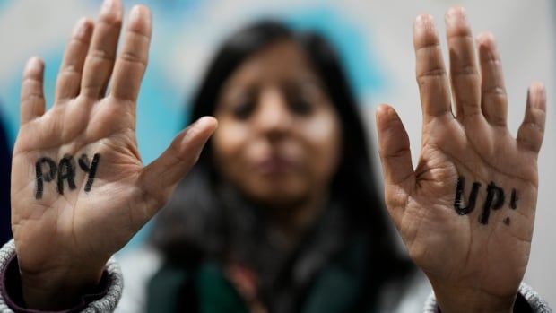 A demonstrators holds up their hands to display the words 'Pay' and 'Up' written on the palms.