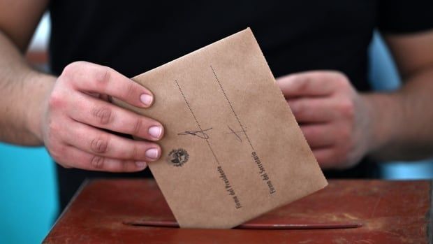 A voter places a ballot into a ballot box.