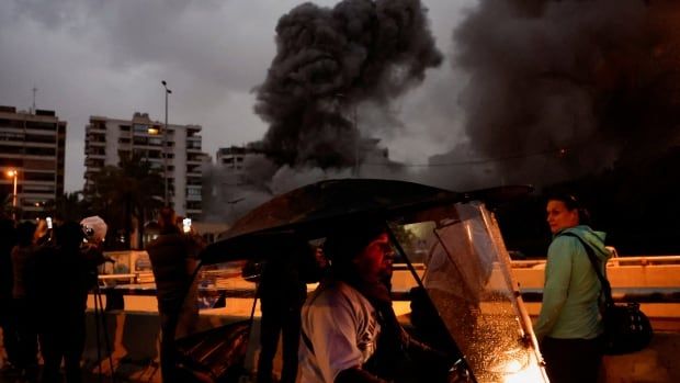 People watch as a strike hits a building and smoke billows over.