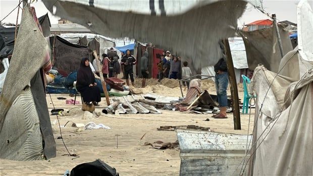 A woman sits in a destroyed encampment on the beach.