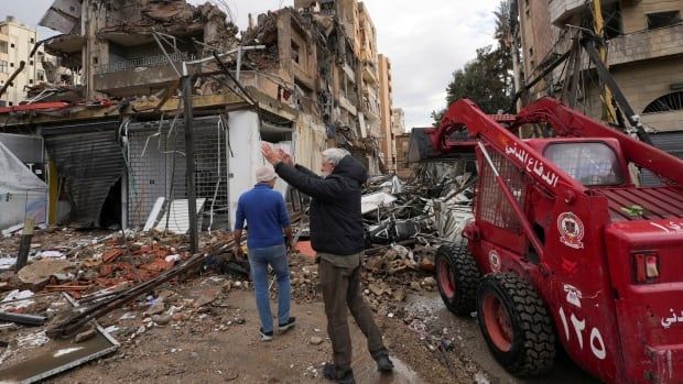 Two men walk through damaged site.