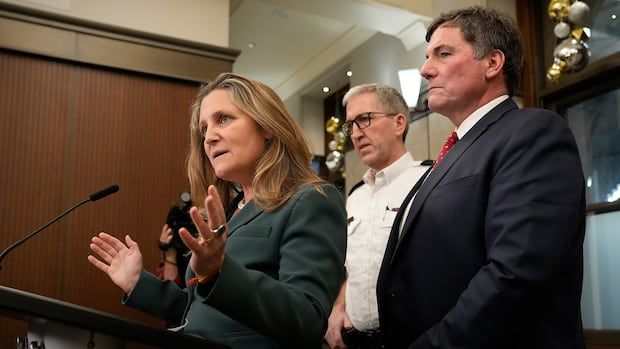 A woman speaks at a podium with two men standing behind her.