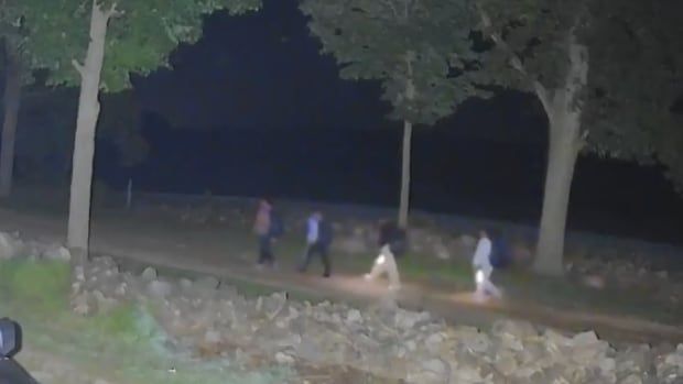 Dark image showing a group of four people walking at night with flashlights.