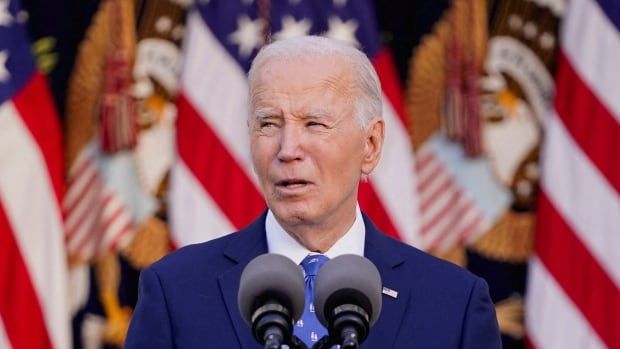 A man in a blue suit speaks from a podium in front of American flags.