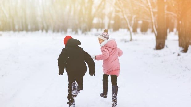 Two kids, a boy and a girl, running through the snow 