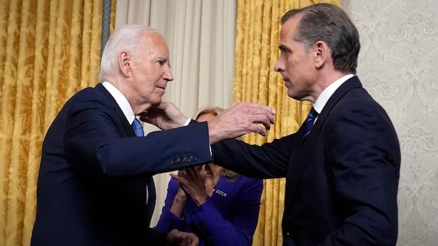 An elderly man in a suit reaches to hug a middle-aged man in a suit inside a formal room. 